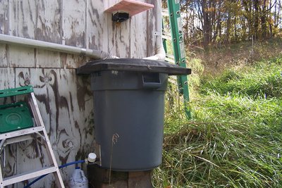 Another view of the rain barrel, showing the camera mount and the external strainer with a pipe cap over its head.  Water line is buried down to here.